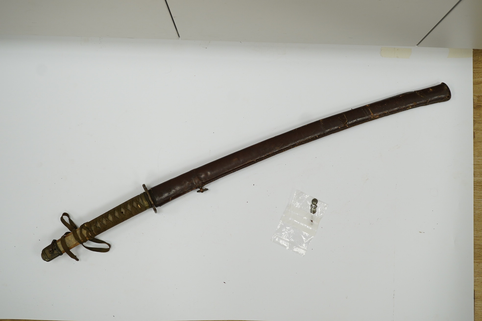 A WWII Japanese army officer’s Shingunto sword katana, blade 66.4cm, signed with Showa to stamp (tip of blade damaged), with unusual brass mounts, in its leather covered combat scabbard. Condition - poor to fair